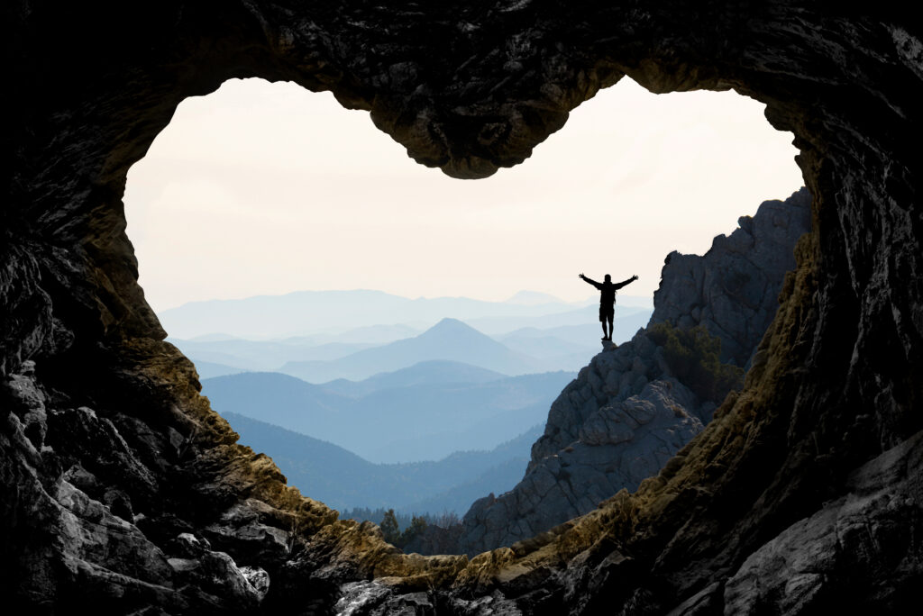 Woman standing with arms outstretched in a heart-shaped rock formation, symbolizing freedom, self-celebration, and the power of pausing to reconnect.